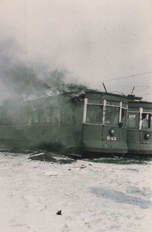 A vintage black and white photo shows a streetcar on fire in the snow, with the number 542 visible on its front.