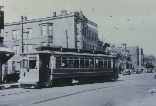A vintage black-and-white photo shows a Chicago Surface Lines streetcar, number 3010, on a city street with 1930s automobiles parked nearby and a brick building in the background.