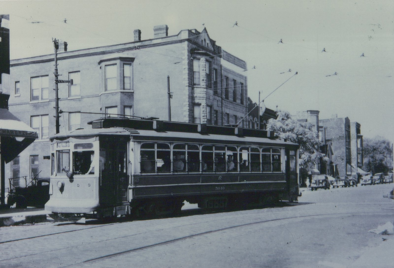 A vintage black-and-white photo shows a Chicago Surface Lines streetcar, number 3010, on a city street with 1930s automobiles parked nearby and a brick building in the background.