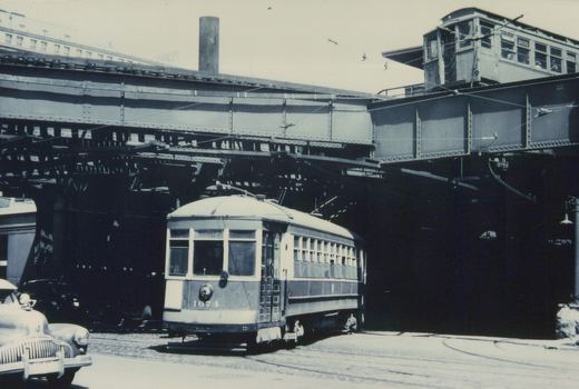 Black-and-white photo of a streetcar numbered 1674 on a city street beneath an elevated train line with a car numbered 2535, located at the corner of Van Buren and Clinton streets in Chicago.