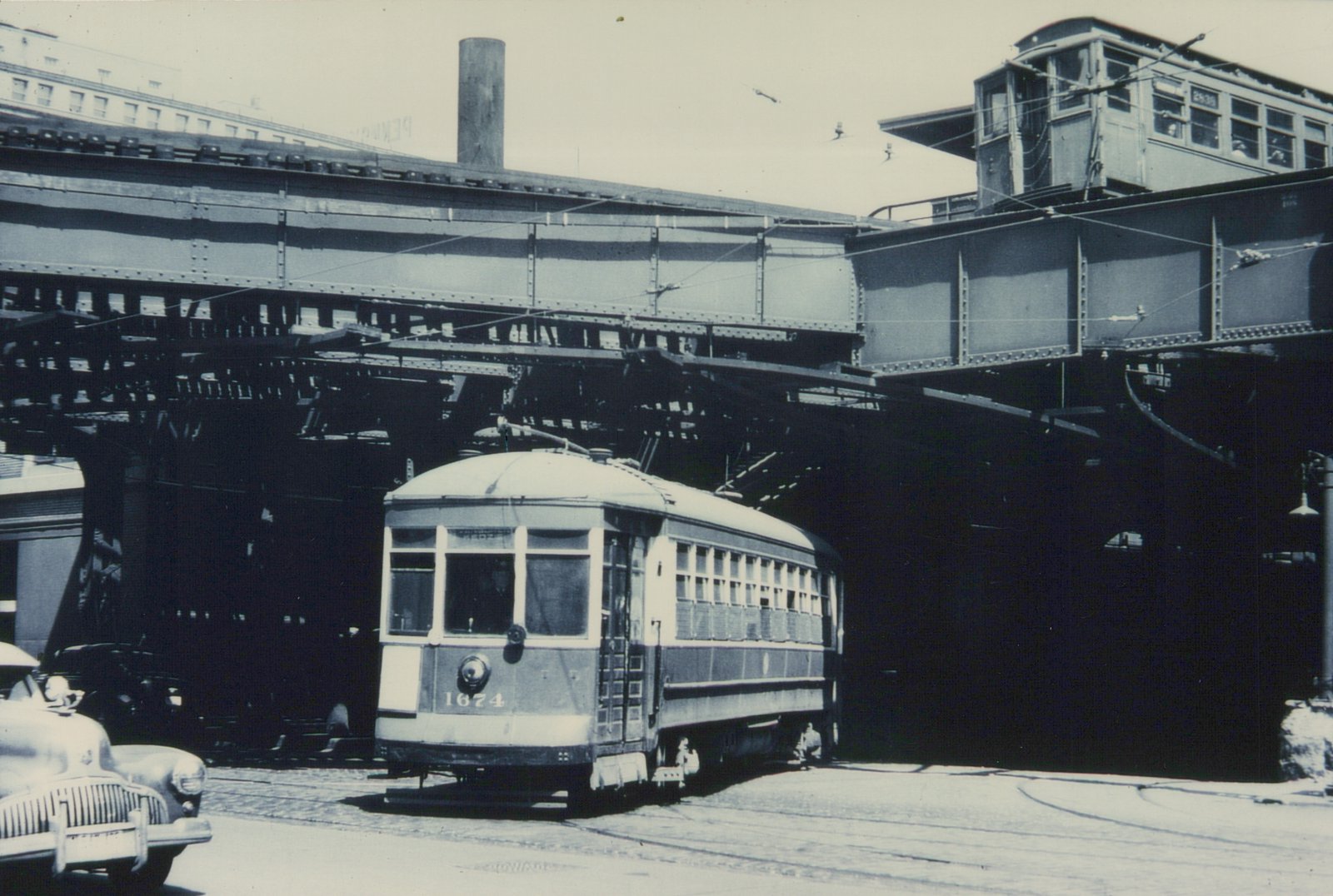 Black-and-white photo of a streetcar numbered 1674 on a city street beneath an elevated train line with a car numbered 2535, located at the corner of Van Buren and Clinton streets in Chicago.
