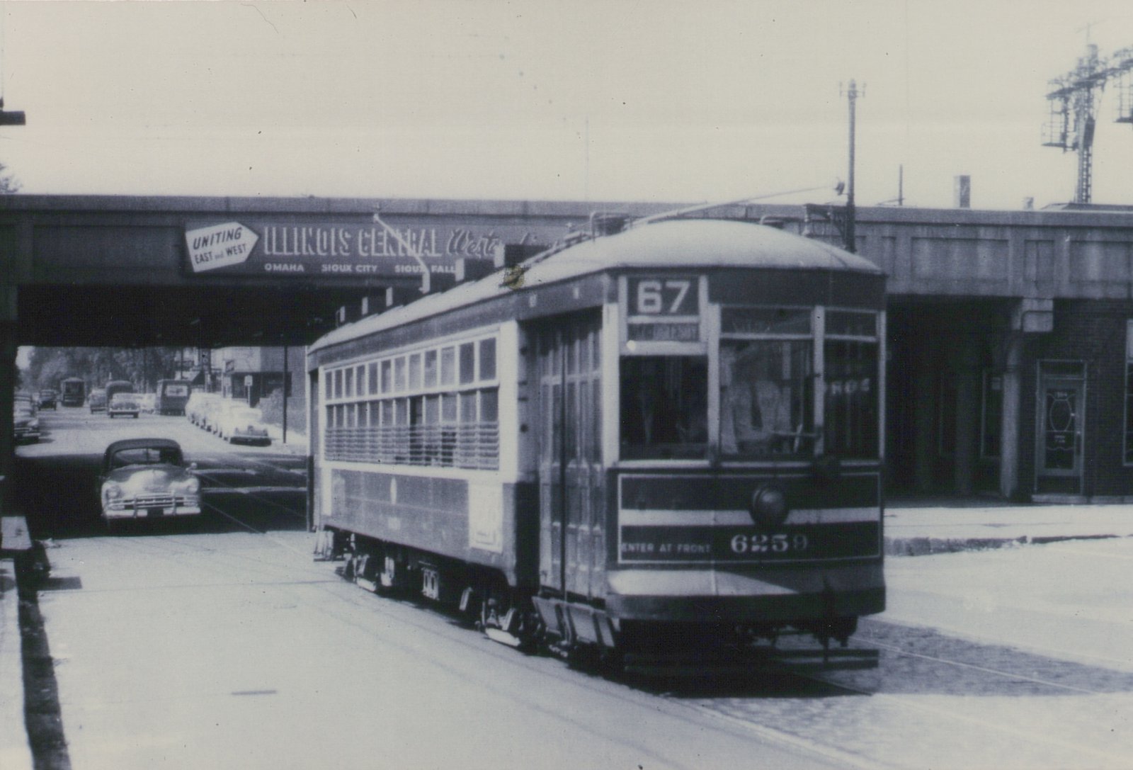 A vintage black and white photograph of a Chicago Surface Lines streetcar on route 67, number 6259, moving along a street under an elevated railroad bridge with an 'Illinois Central West' sign.