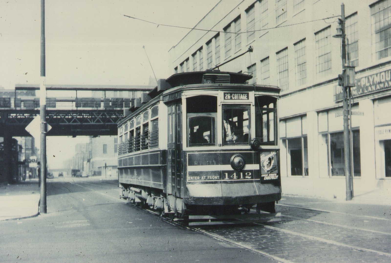 A black and white photograph shows a vintage Chicago streetcar on a city street with an elevated railway overhead and a large building in the background. The car is numbered 1412 and displays the route 26-Cottage.