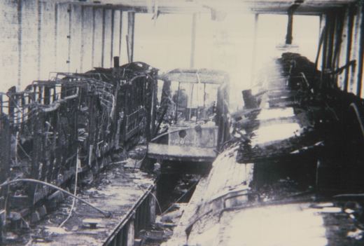 A black-and-white photo shows the burned-out interior of a carbarn, featuring the front of a streetcar numbered 268, surrounded by charred debris and twisted metal.