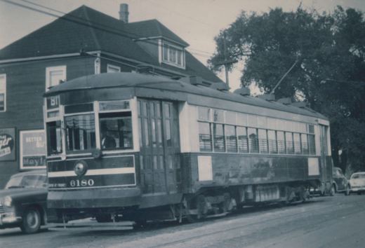 A vintage black-and-white photo of a Chicago Surface Lines streetcar, number 6180, with a trolley pole, running on a city street with cars and a building in the background.