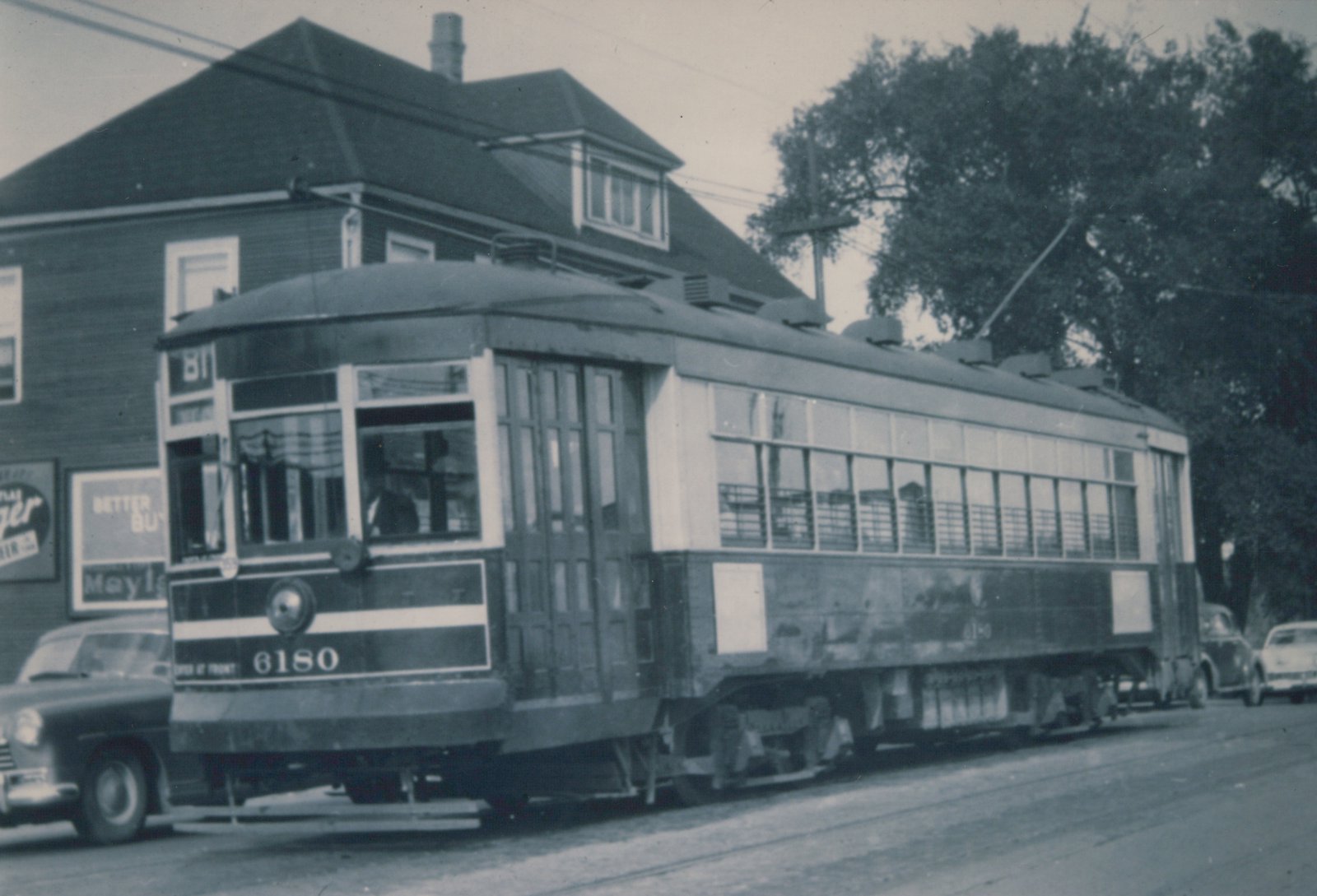 A vintage black-and-white photo of a Chicago Surface Lines streetcar, number 6180, with a trolley pole, running on a city street with cars and a building in the background.