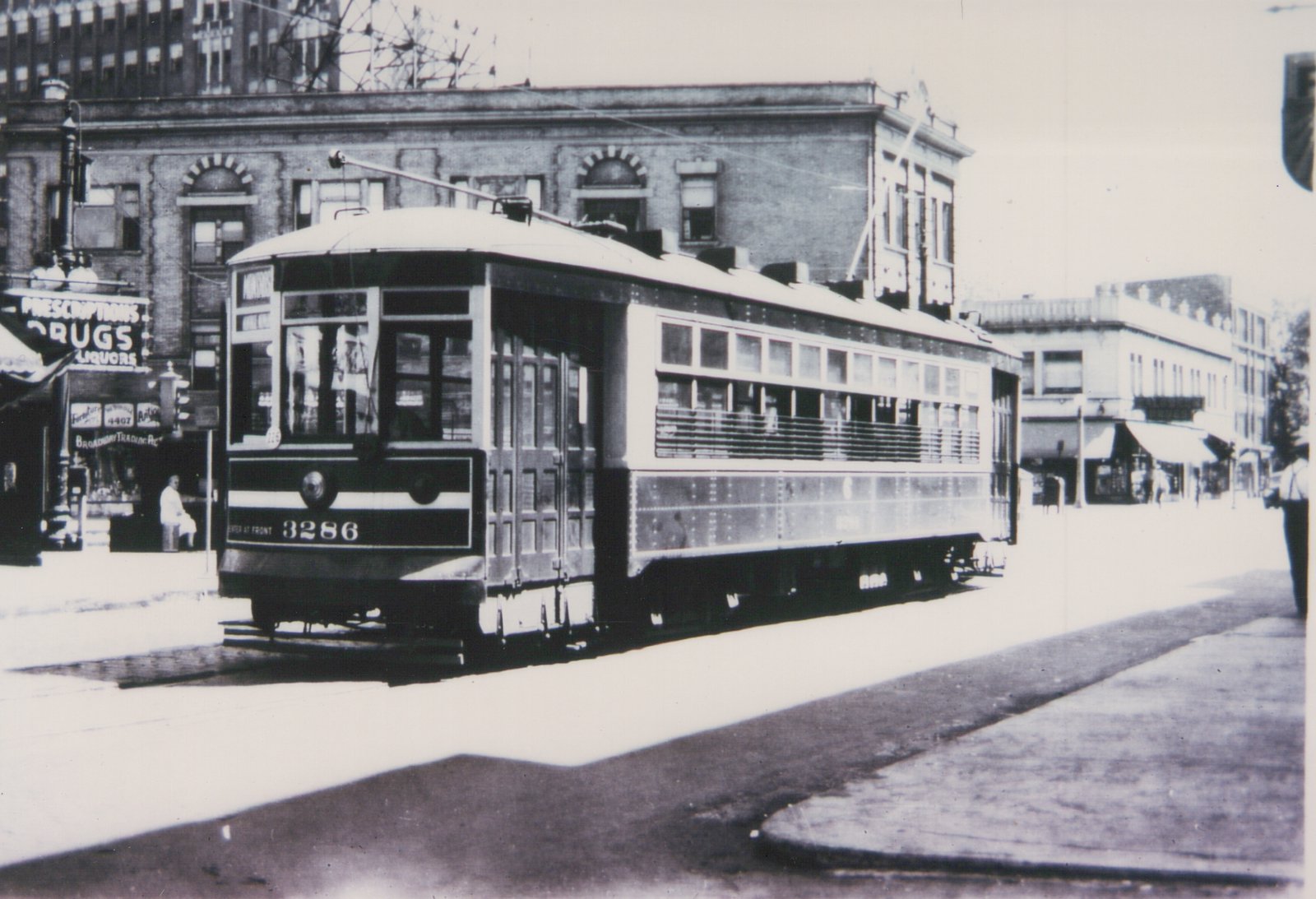 A black-and-white photo of a vintage streetcar numbered 3286 on a city street, with a drugstore and other storefronts visible behind it.