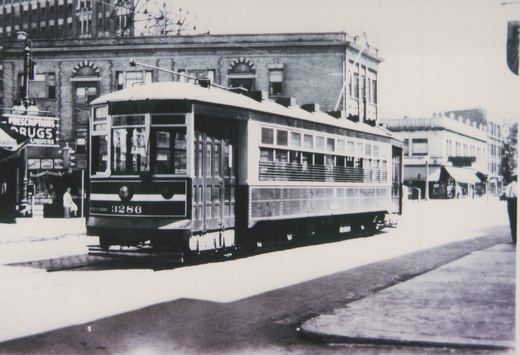 A black-and-white photo of a vintage streetcar numbered 3286 on a city street, with a drugstore and other storefronts visible behind it.