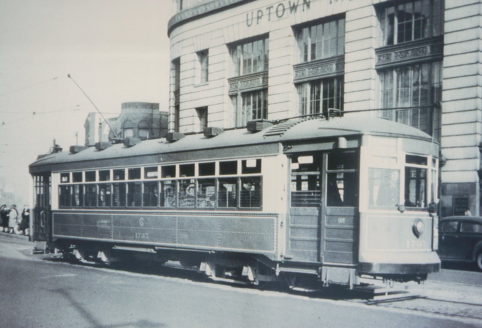 A vintage black and white photo of a Chicago streetcar numbered 1735, with several people near it and a car parked alongside, in front of a building labeled UPTOWN.
