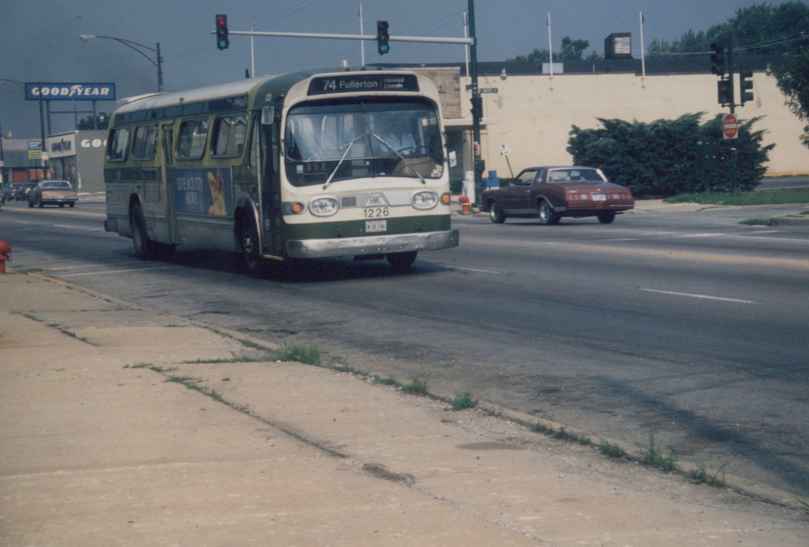 A green and cream CTA bus numbered 1226 is turning at a street intersection with traffic lights and other cars visible, under a clear sky.