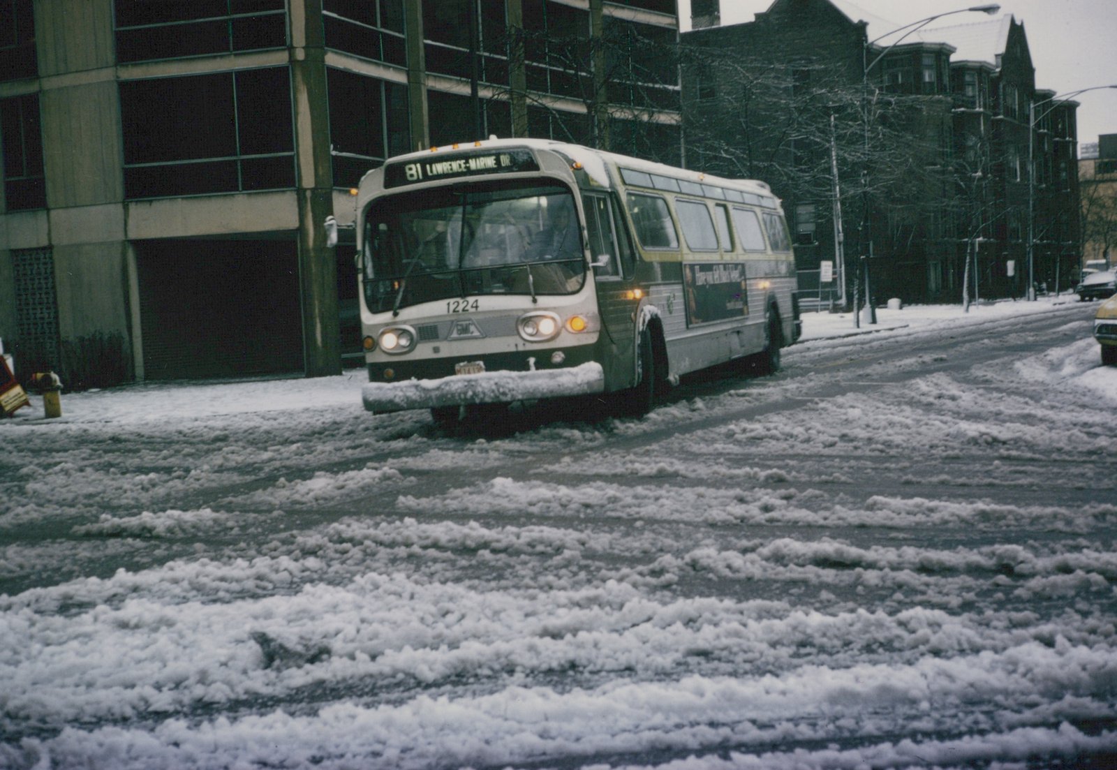 A white and green bus with the number 1224 drives down a snow-covered street in Chicago, with buildings and bare trees in the background.