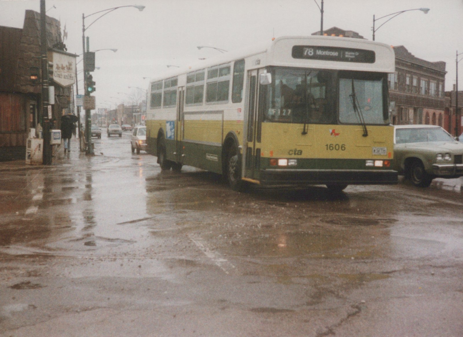 A yellow and green CTA bus with the number 1606 on the front is stopped on a wet street with cars and a building in the background.