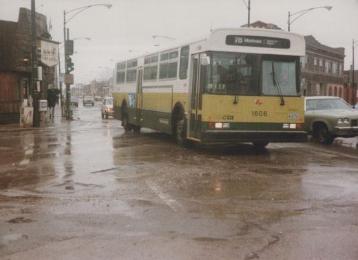 A yellow and green CTA bus with the number 1606 on the front is stopped on a wet street with cars and a building in the background.