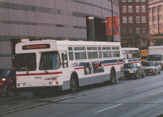 A white Chicago Transit Authority bus, number 1600, is shown on a city street with a '125 Water Tower Express Chestnut' sign on its front, surrounded by cars and a motorcycle.