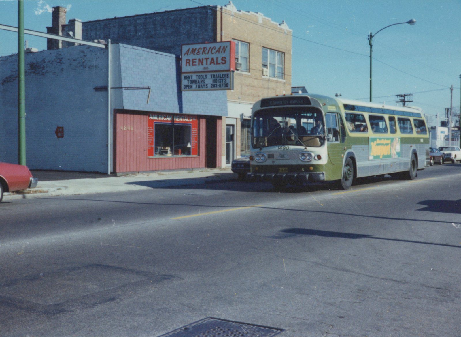 A green and cream Chicago Transit Authority bus, number 1490, drives down a city street on a clear day, with a storefront for 'American Rentals' visible in the background.