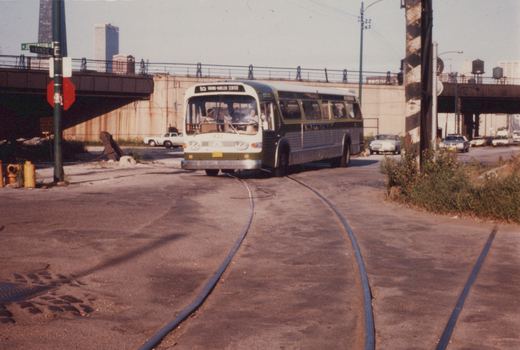 A green and cream CTA bus with the number 1422 is driving on a street next to train tracks, with a street sign for Jefferson and Kinzie Streets visible and a bridge in the background.