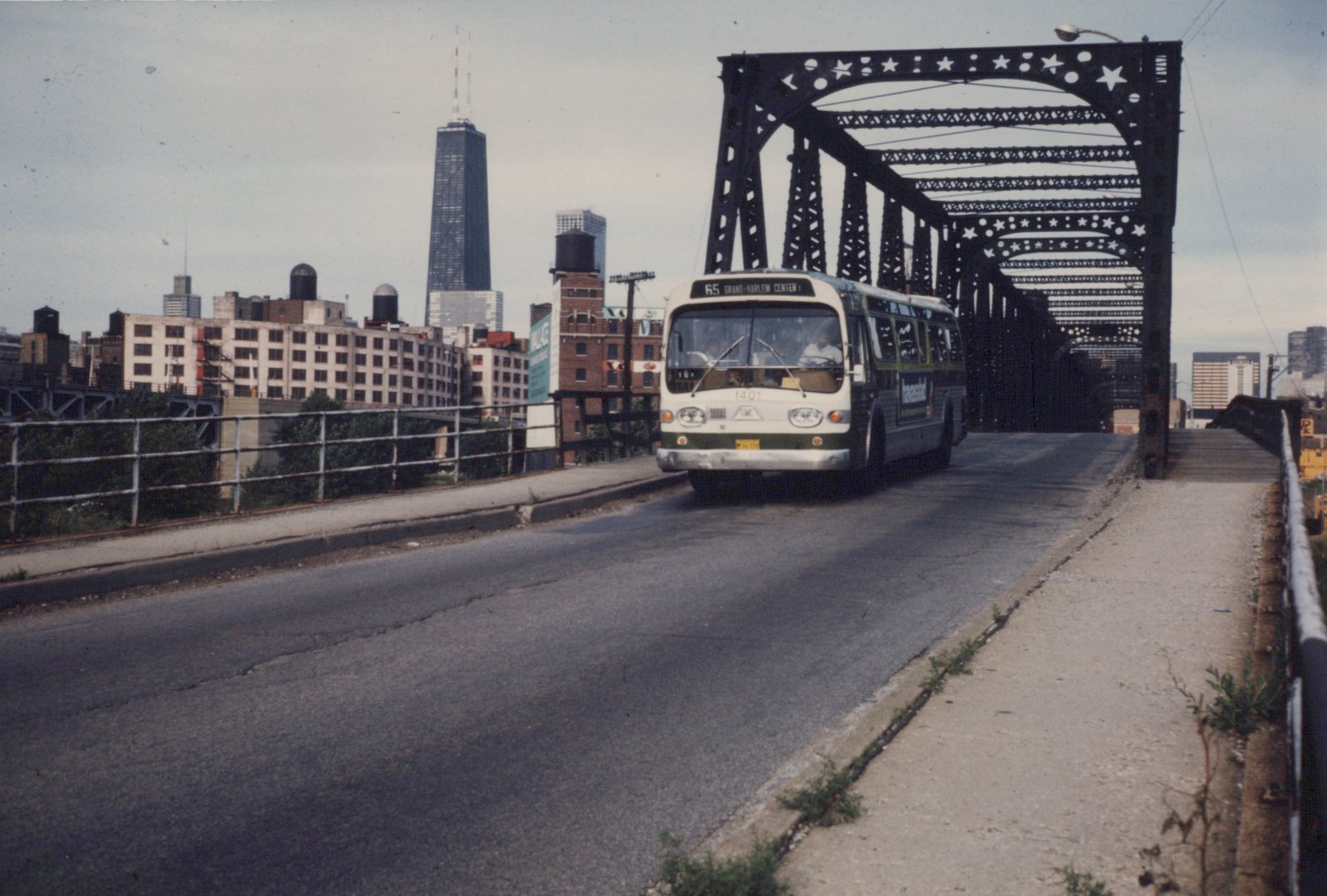 A white and green CTA bus, number 1401, driving over a black metal bridge in Chicago. The Hancock Building is visible in the skyline.