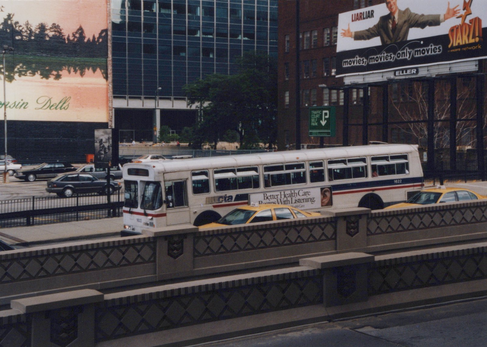 A white Chicago Transit Authority bus with the number 1622 is shown on a bridge, with a yellow taxi below and billboards advertising 'Liar Liar' and 'Starz!' in the background.