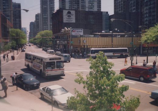 A white CTA bus marked 1622 is driving down a city street in Chicago, surrounded by cars and pedestrians near the Clark and Broadway intersection with tall buildings in the background.