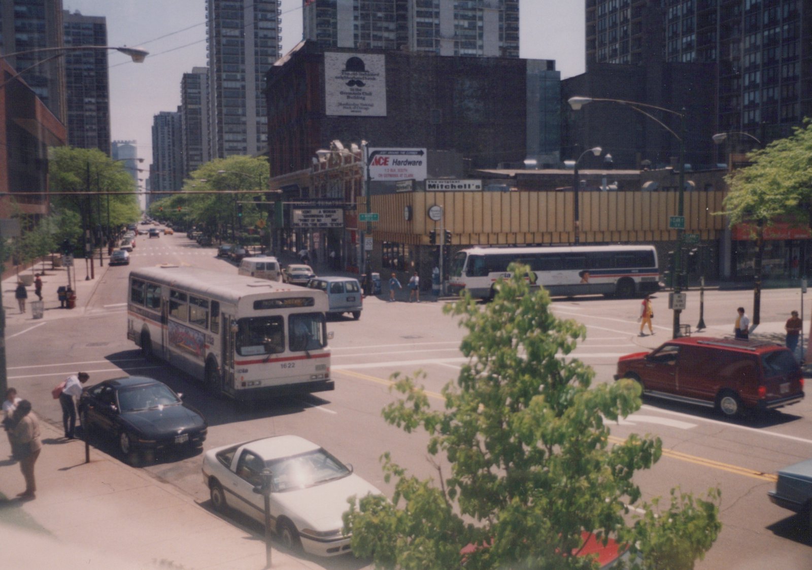 A white CTA bus marked 1622 is driving down a city street in Chicago, surrounded by cars and pedestrians near the Clark and Broadway intersection with tall buildings in the background.