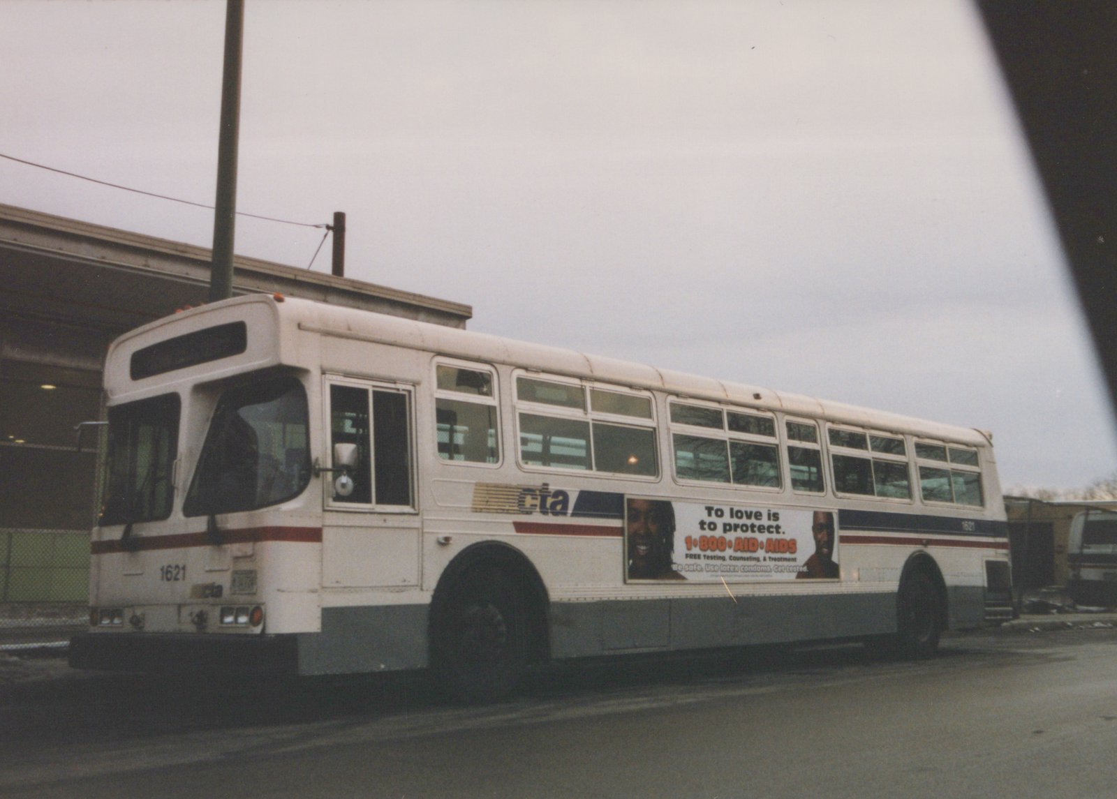 Side view of a white Chicago Transit Authority bus numbered 1621, showing an AIDS awareness ad on its side, parked on a wet street under an overcast sky.