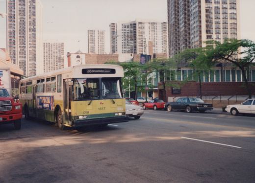 A green and cream CTA bus with the number 1617 and route 36 Broadway is on a city street with tall buildings and several cars from the 1980s in the background.
