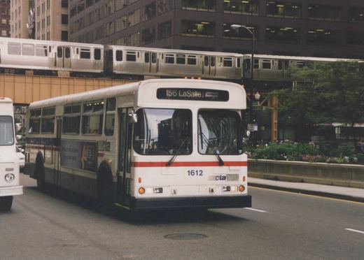 A white CTA bus with red and blue stripes is on a city street, with a silver 'L' train on an elevated track above it.
