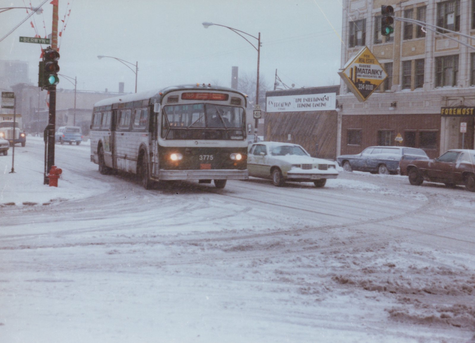 A white and black Chicago Transit Authority bus with the number 3775 is driving on a snow-covered street in Berwyn, Illinois, with other cars parked along the side.