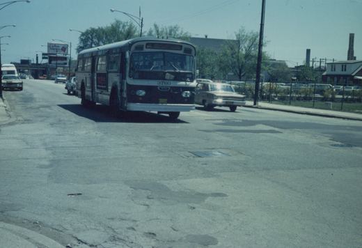 A maroon and white Chicago Transit Authority bus with the number 3760 moves down a sunny city street, surrounded by 1960s cars and storefronts.