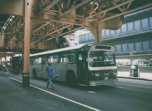 A green and cream CTA bus numbered 3706 is parked under a large steel elevated train structure. A person walks in front of the bus, and a black steam locomotive is visible in the background.