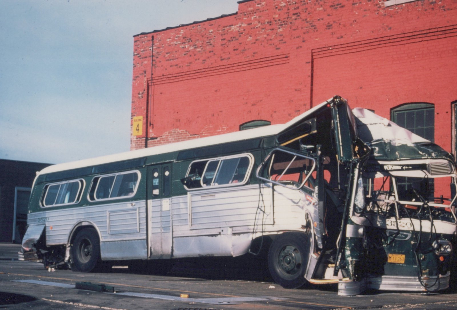 A side view of a green and white CTA bus with its front end crushed, parked on a street in front of a red brick building.