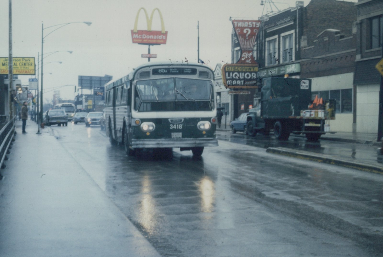 Front view of a green and white Chicago Transit Authority bus driving on a wet street with people on the sidewalk and a McDonald's sign in the background.