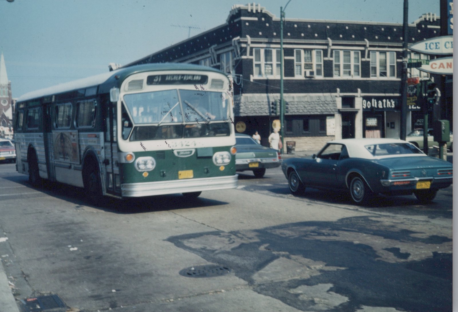 A green and white CTA bus drives down a city street with vintage cars and pedestrians, with a street sign for Halsted Street visible.