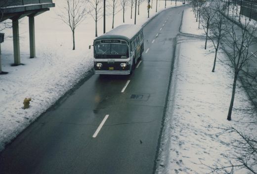A green and white bus with the number 3352 and destination 'HARRISON-CENTRAL' drives on a wet, snow-lined road under an overpass.
