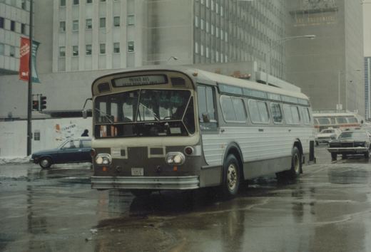 A white and dark-colored CTA bus with the number 3314 is driving down a wet city street with tall buildings in the background, including one with a sign for The Prudential.