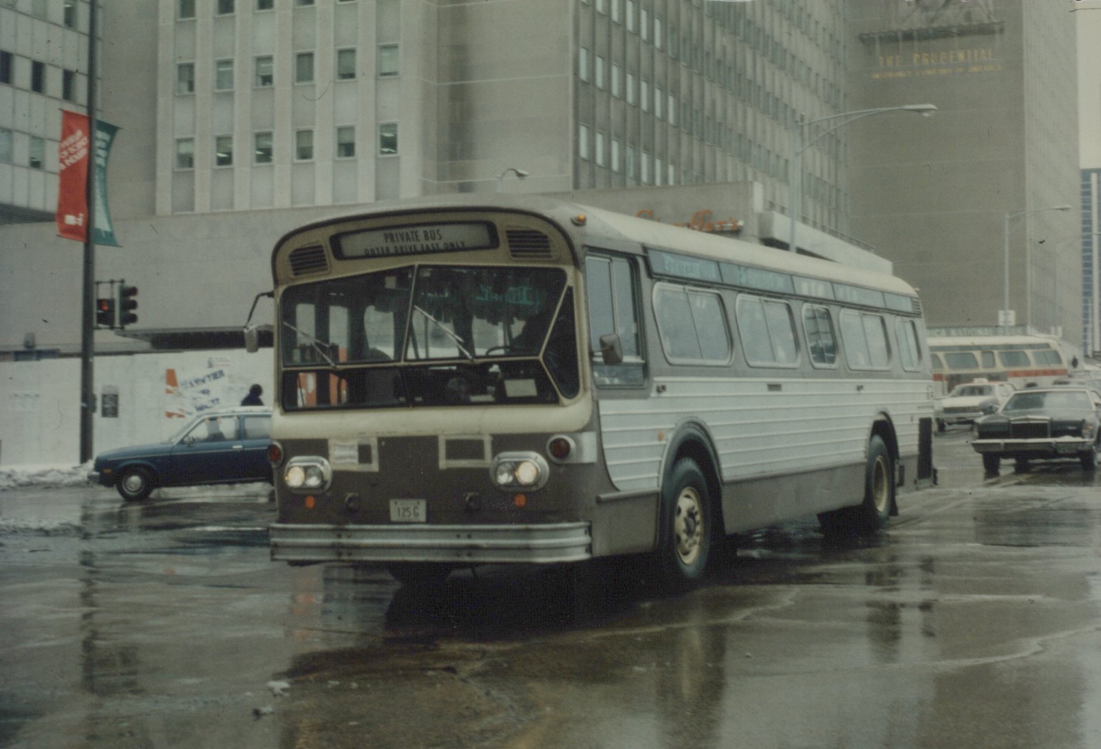 A white and dark-colored CTA bus with the number 3314 is driving down a wet city street with tall buildings in the background, including one with a sign for The Prudential.
