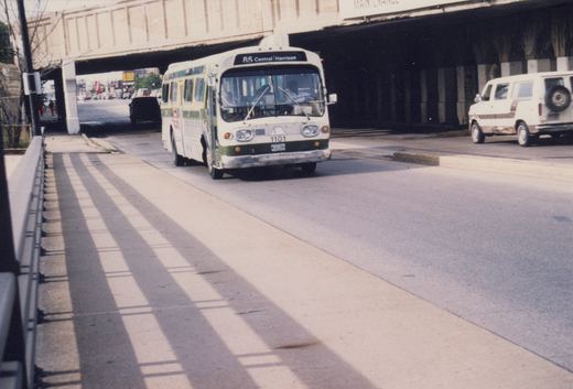 A white and green Chicago Transit Authority bus, number 1101, is driving on a street under a concrete overpass on a clear day.