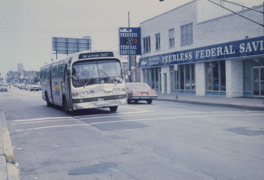 A white and green CTA bus, number 1100, drives on a city street past a red car and a building with a sign for Peerless Federal Savings.