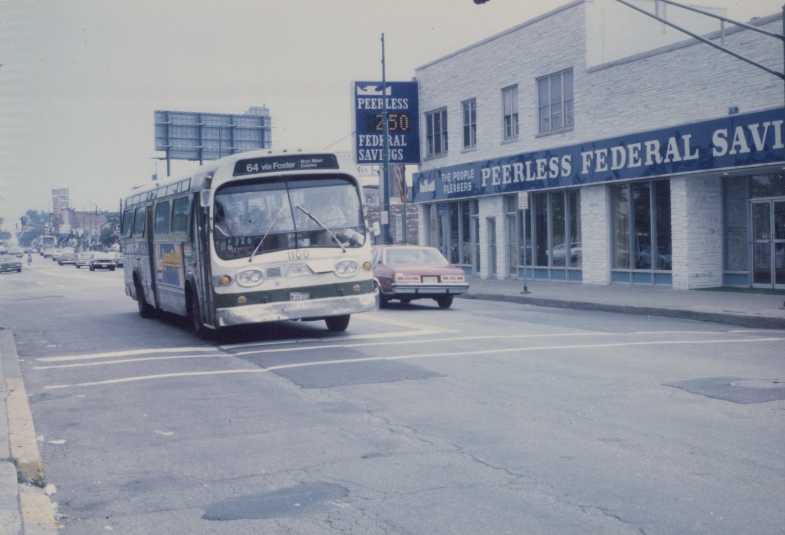 A white and green CTA bus, number 1100, drives on a city street past a red car and a building with a sign for Peerless Federal Savings.
