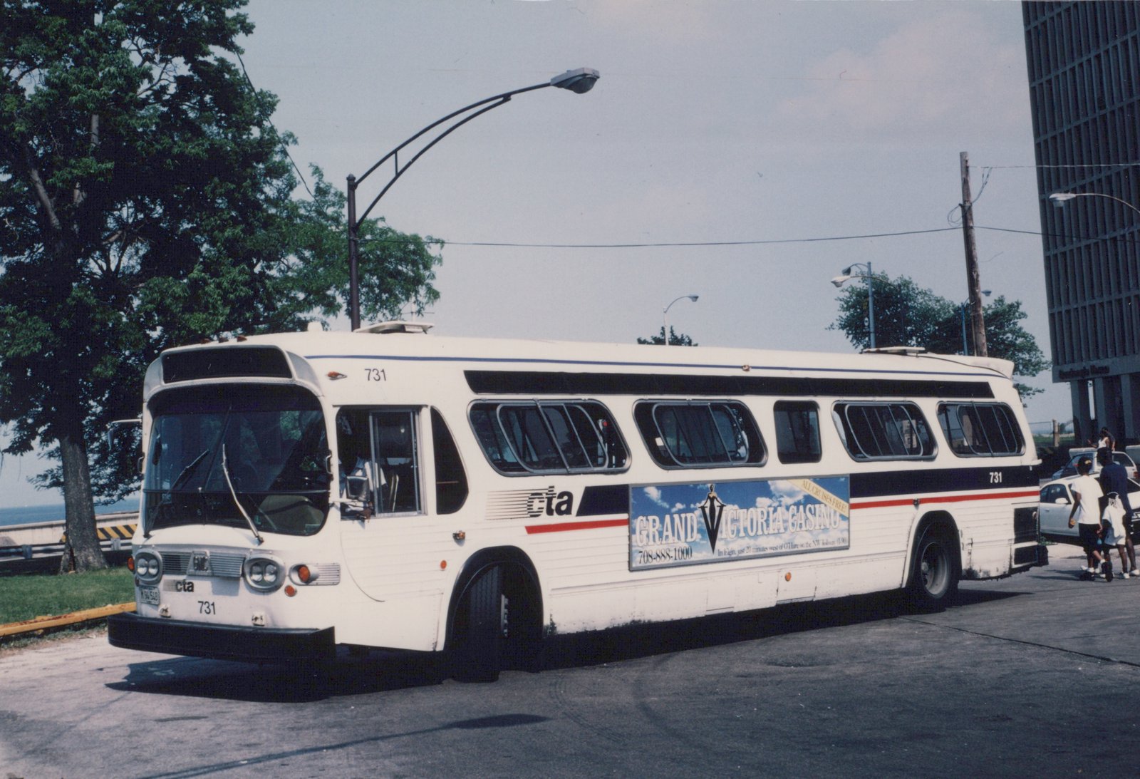 A white CTA motor bus numbered 731, displaying an advertisement for Grand Victoria Casino, is parked on a street with people walking nearby.