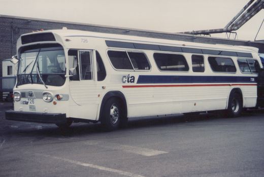 A white CTA bus with blue and red stripes, number 726, is parked in a lot with a brick building behind it.