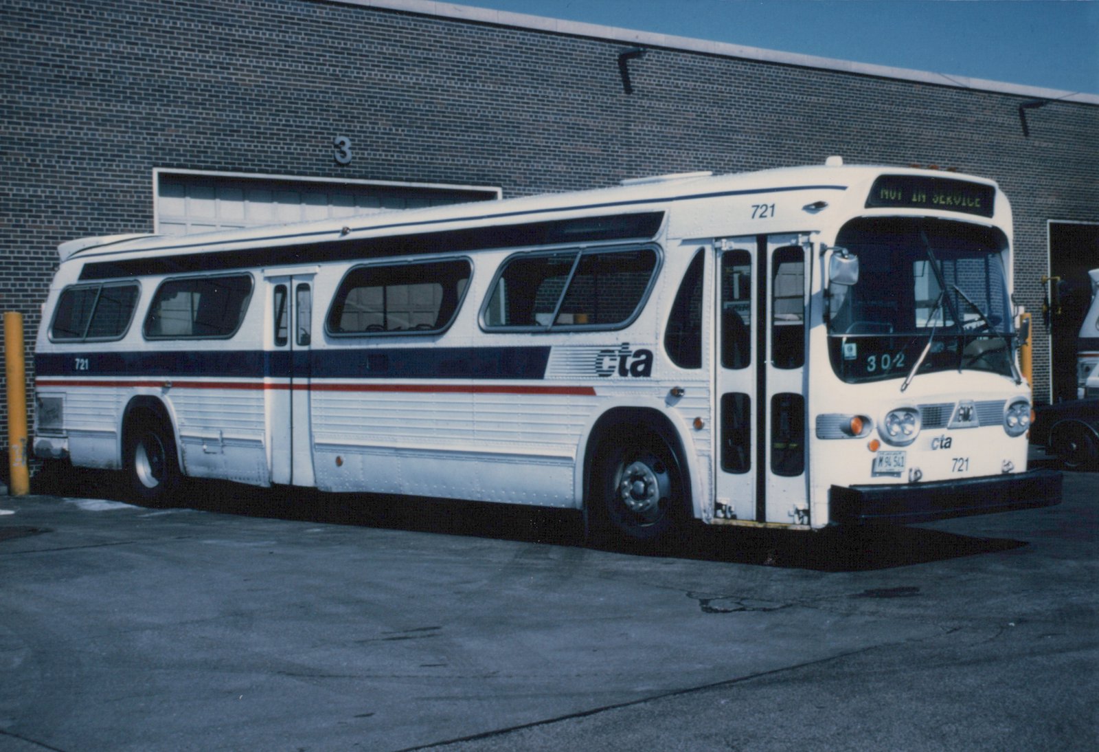 A white CTA bus with blue and red stripes, numbered 721 and built by GMC, is parked in a garage with its front sign showing 'NOT IN SERVICE'.