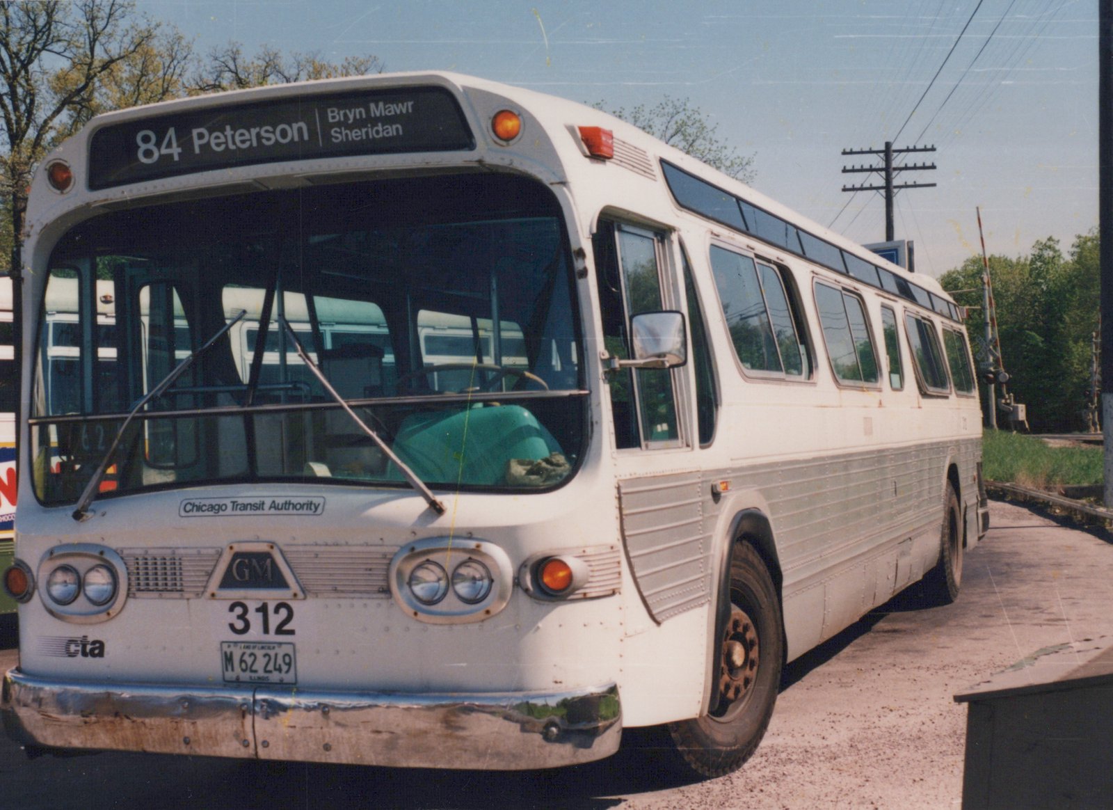 A white and silver CTA bus number 312 is parked on a city street beside railroad tracks under a clear blue sky, with its destination sign reading "84 Peterson".