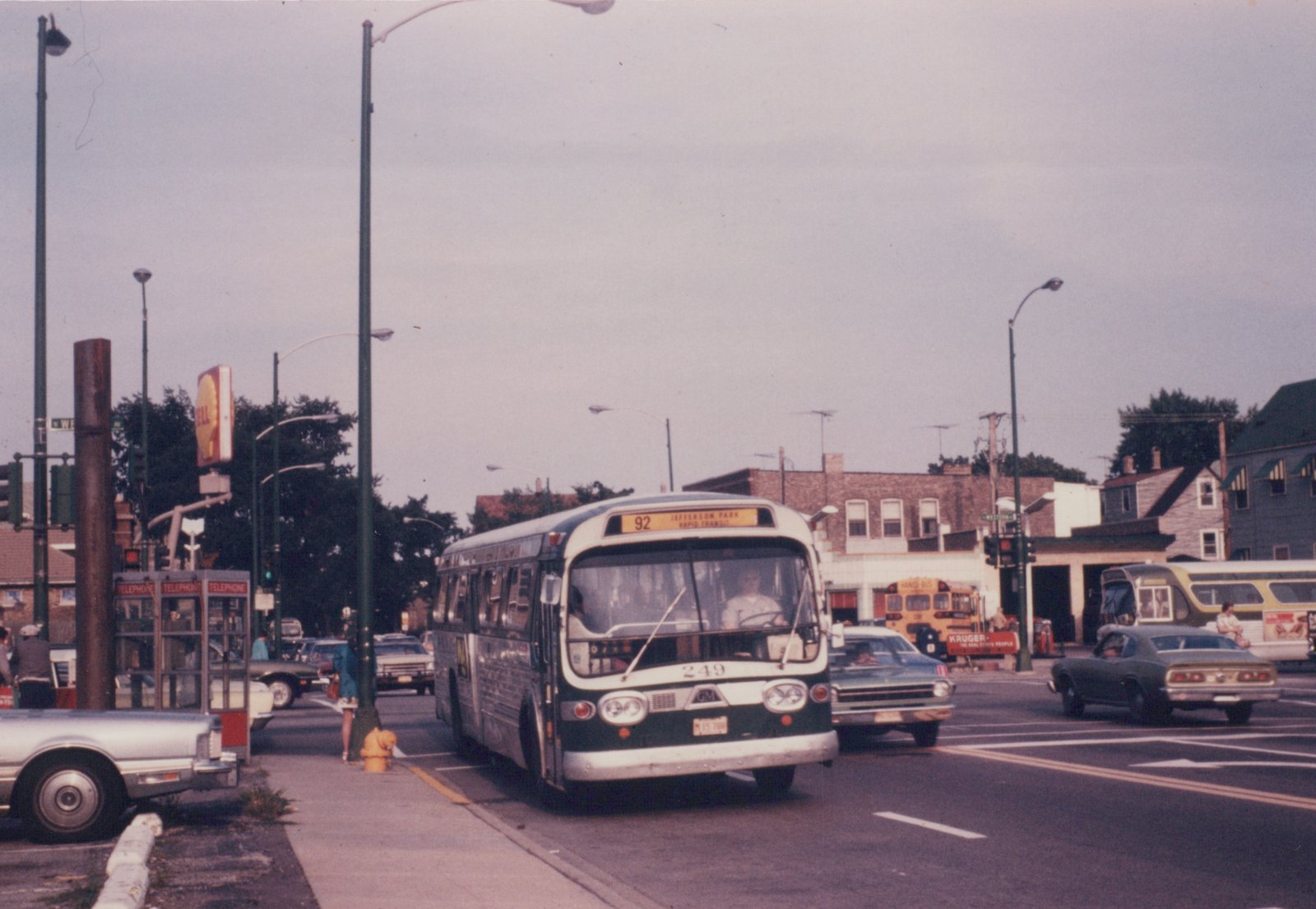 A green and white Chicago Transit Authority bus on a city street with cars and a phone booth in the background.