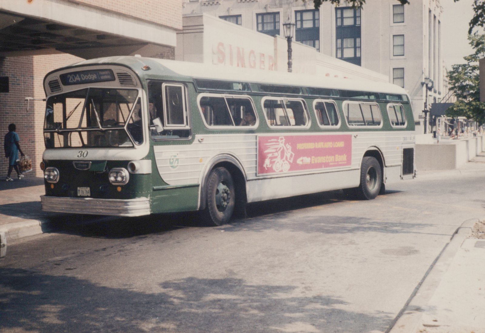A green and white Chicago Transit Authority motor bus, number 30, is parked on a city street with a pink advertisement for The Evanston Bank on its side.