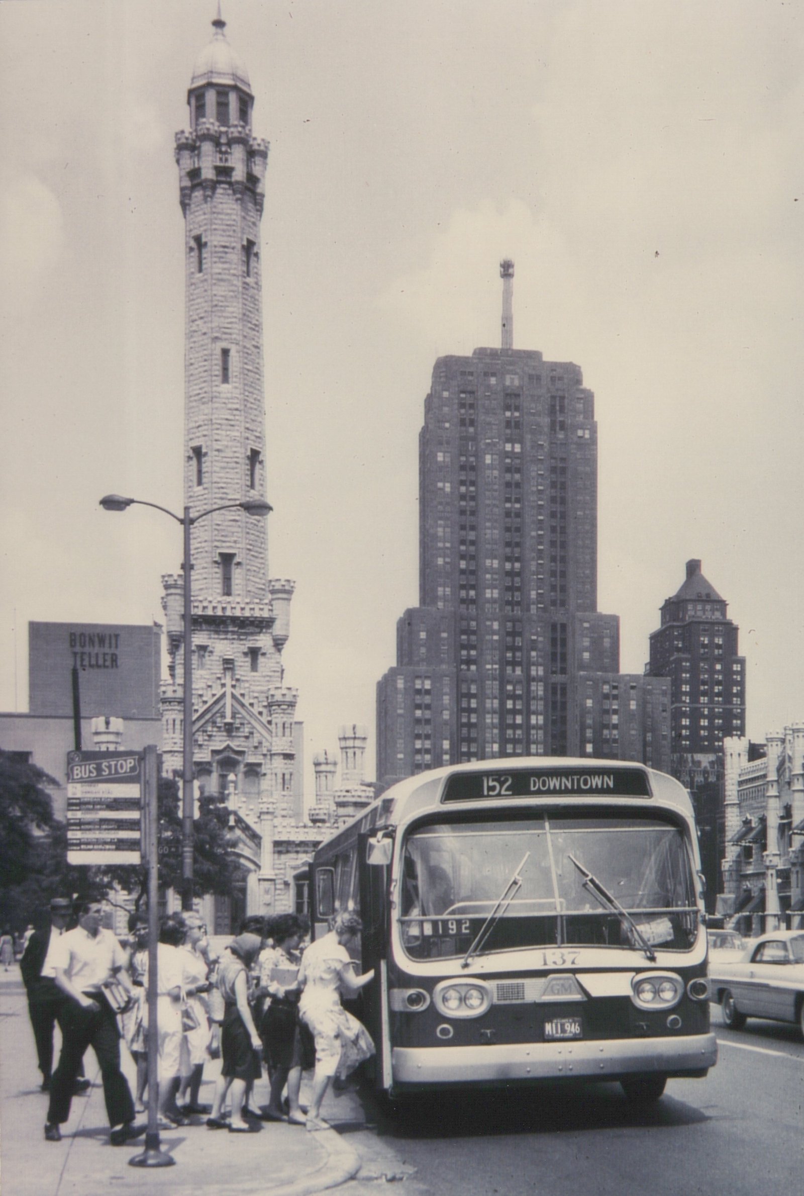 A black and white photo of a CTA bus numbered 137 on a city street, with passengers boarding. The Chicago Water Tower and a tall building are visible behind it.