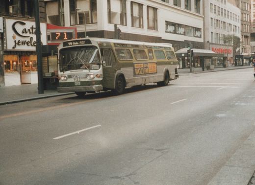 A green and cream Chicago Transit Authority bus, numbered 1143, is stopped at an intersection on a city street with storefronts in the background.
