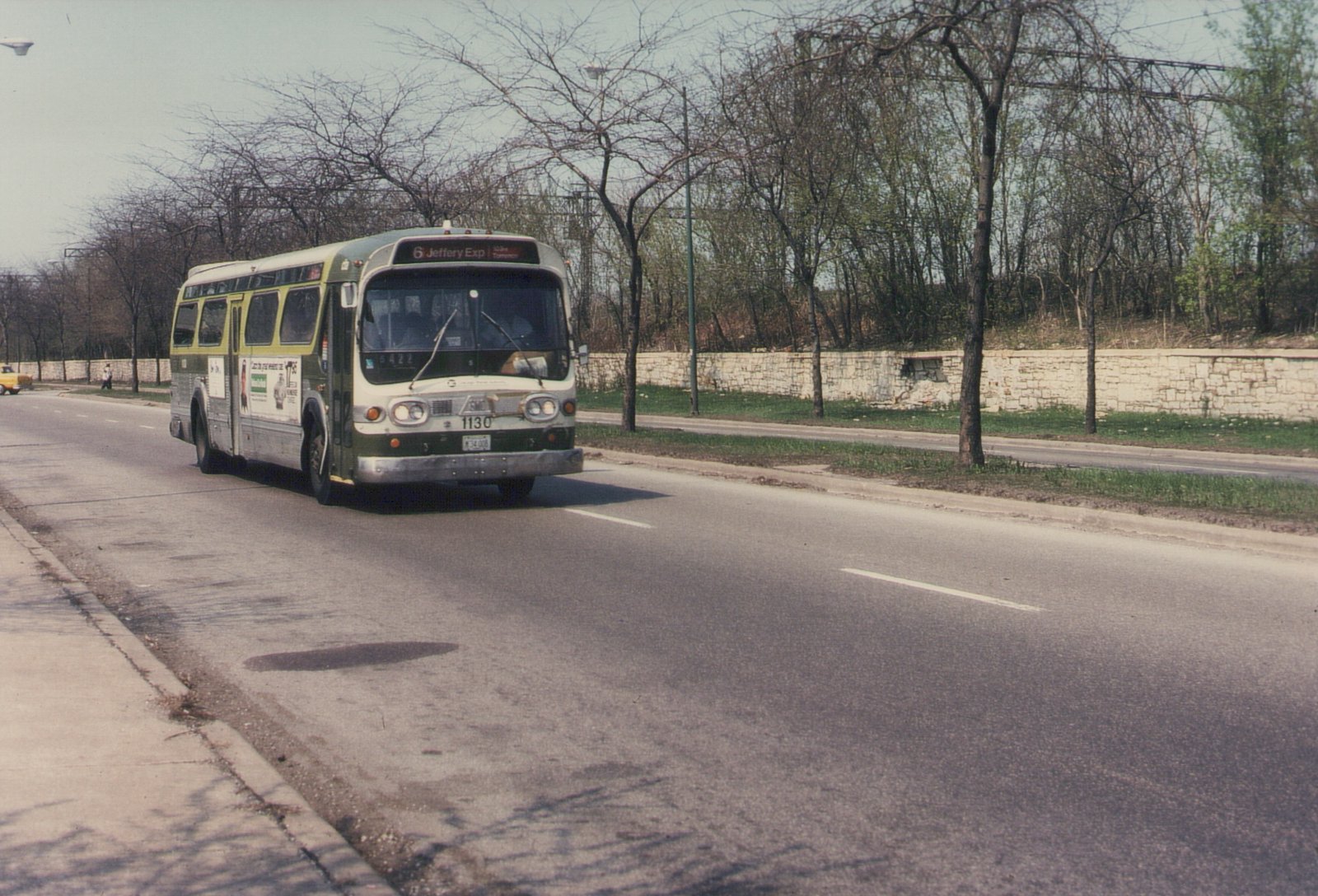 A green and cream CTA motor bus with the number 1130 and destination sign reading '6 Jeffery Exp' drives down a tree-lined street on a clear day.