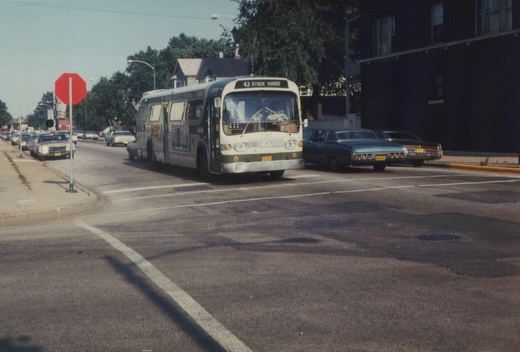A green and cream CTA bus numbered 1147, displaying route 43 to Stock Yards, is stopped at a street intersection with several cars and a stop sign visible.