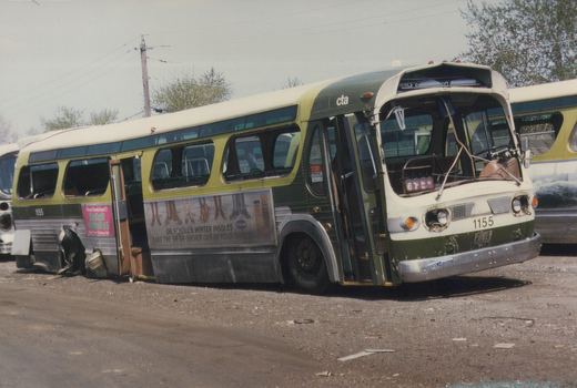 A green and cream CTA bus, number 1155, parked in a gravel yard with visible damage to its rear and side, showing a route 62 sign and advertisements.